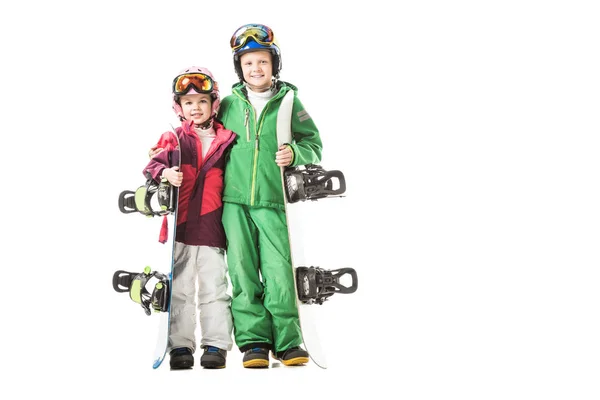 Hermana y hermano de pie con tablas de snowboard en trajes de nieve aislados en blanco - foto de stock