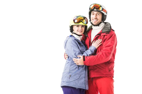 Paar in Skianzügen, Schutzbrille und Helm umarmen sich, lächeln und blicken vereinzelt in die Kamera — Stockfoto