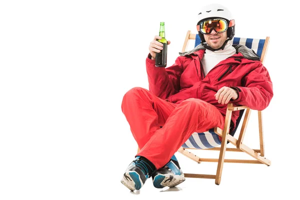 Hombre feliz en traje de esquí rojo con botella de cerveza sentado en la silla de cubierta y sonriendo aislado en blanco - foto de stock