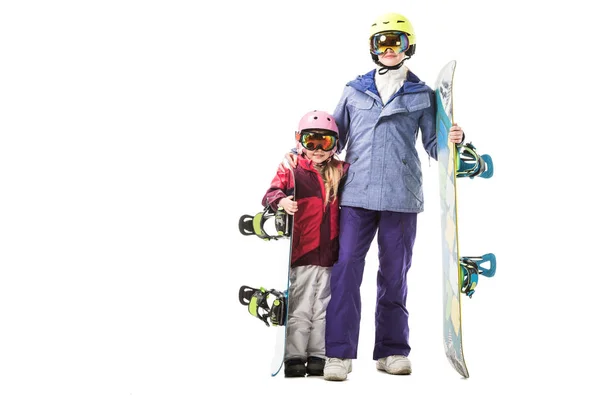 Mamá e hija preescolar en trajes de esquí, gafas y cascos con tablas de snowboard sonriendo aisladas en blanco - foto de stock