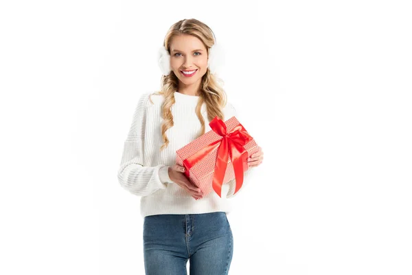 Красива усміхнена молода жінка в зимовому вбранні тримає подарунок ізольовано на білому — стокове фото