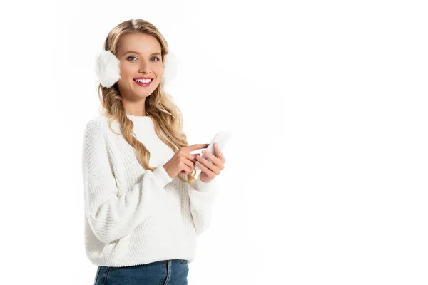 Atractiva chica sonriente en orejeras usando teléfono inteligente aislado en blanco - foto de stock