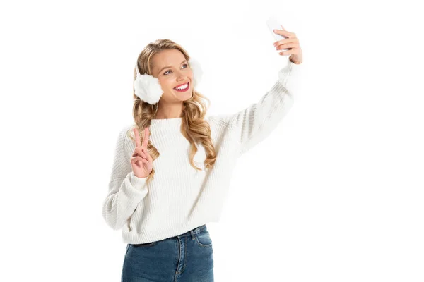 Весела дівчина показує знак перемоги, приймаючи селфі на смартфон ізольовано на білому — стокове фото