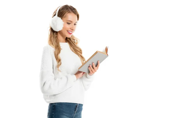 Mujer atractiva alegre en orejeras blancas libro de lectura aislado en blanco - foto de stock