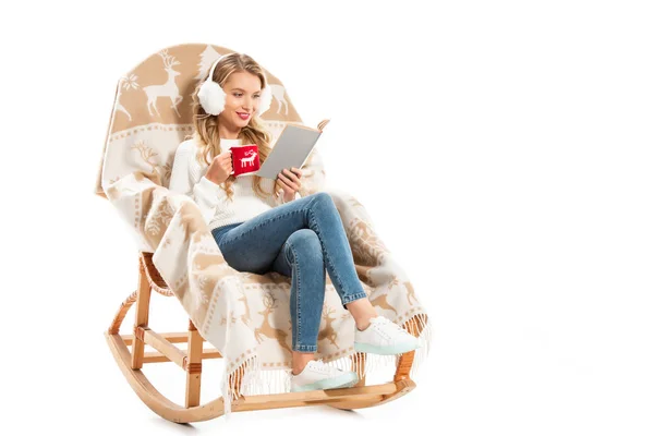 Glückliches Mädchen mit einer Tasse Kaffee, das Buch liest, während es im Schaukelstuhl isoliert auf weiß sitzt — Stockfoto