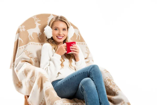 Щаслива молода жінка тримає чашку на каві, сидячи в кріслі, ізольованому на білому — стокове фото