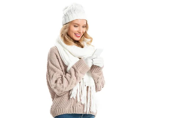 Mujer rubia alegre en suéter de invierno y sombrero usando teléfono inteligente aislado en blanco - foto de stock