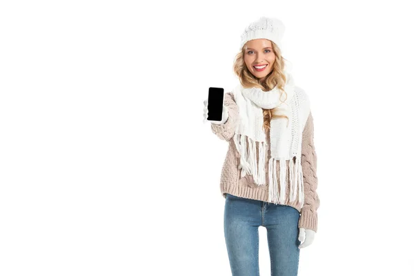 Hermosa mujer sonriente en traje de invierno mostrando teléfono inteligente con pantalla en blanco aislado en blanco - foto de stock