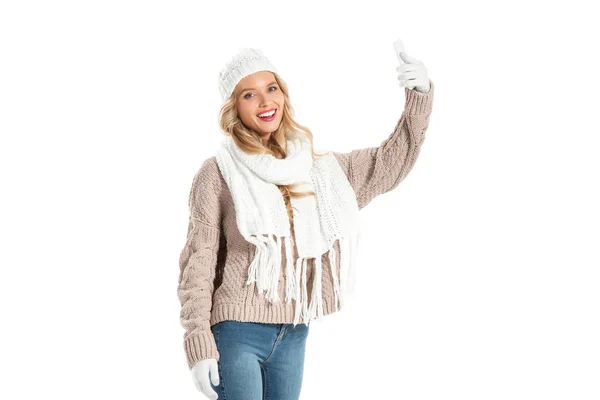 Молодая улыбающаяся женщина в зимнем свитере делает селфи на смартфоне, изолированном на белом — стоковое фото