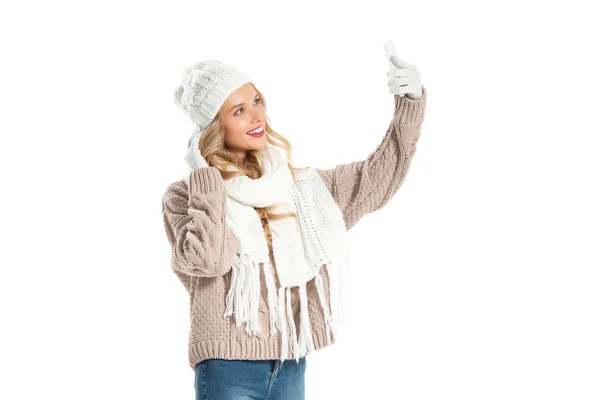 Beautiful young woman in winter outfit taking selfie on smartphone isolated on white — Stock Photo