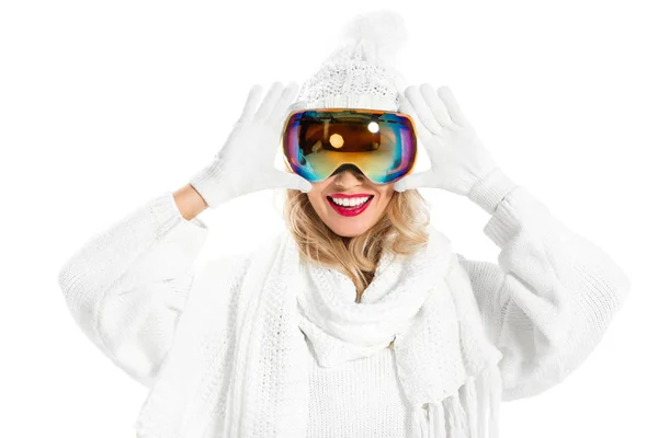 Cheerful woman in white knitted sweater, hat and mittens putting on ski goggles isolated on white — Stock Photo