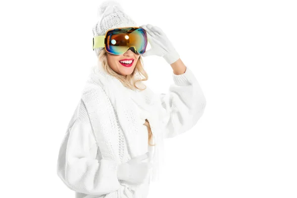 Fröhliche Frau in weißem Strickpullover, Mütze und Fäustlingen, die sich eine Skibrille aufsetzt — Stockfoto