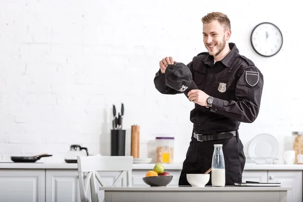 Beau policier avec casquette dans les mains souriant à la cuisine — Photo de stock