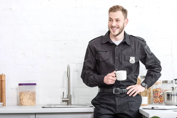 Oficial de policía guapo bebiendo café en la cocina - foto de stock