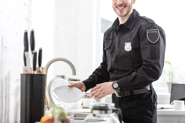 Cropped view of handsome policeman washing plate at kitchen — Stock Photo