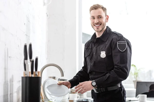 Oficial de policía guapo lavando platos en la cocina - foto de stock