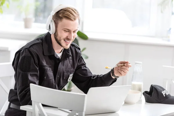 Handsome police officer having breakfast and listening to music with headphones at kitchen table — Stock Photo