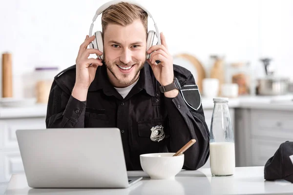 Policier souriant petit déjeuner et écouter de la musique avec écouteurs à la table de cuisine — Photo de stock