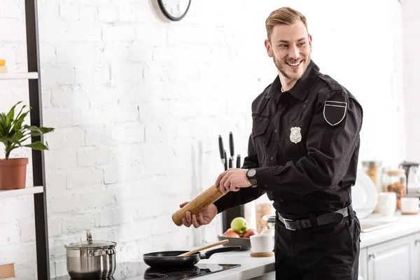 Oficial de policía sonriendo y cocinando desayuno en la cocina - foto de stock