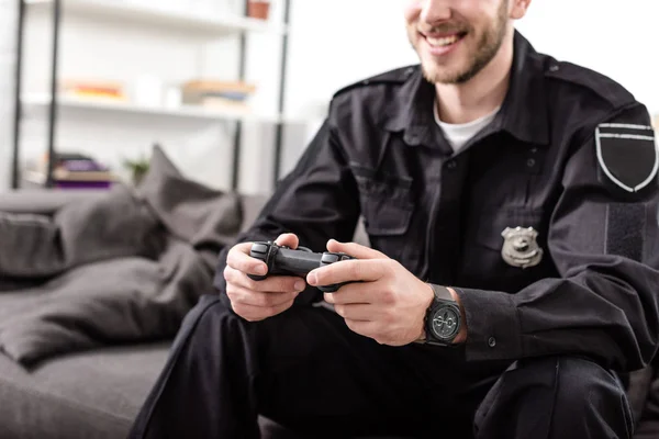 Изображение полицейского с геймпадом, сидящего на диване и играющего в видеоигру — стоковое фото
