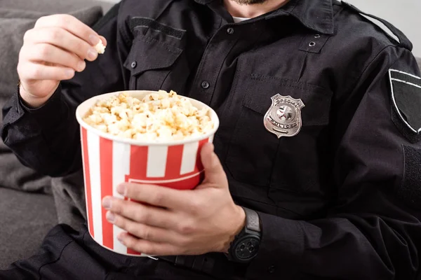 Обрізаний вид поліцейського сидить на дивані і їсть попкорн — стокове фото