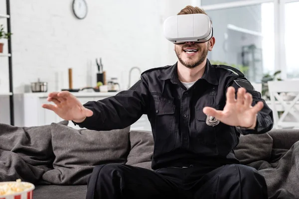 Полицейский с наушниками виртуальной реальности на голове, играющий в видеоигру на диване — стоковое фото
