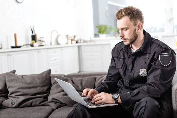 Handsome police officer sitting on couch and typing on laptop keyboard — Stock Photo