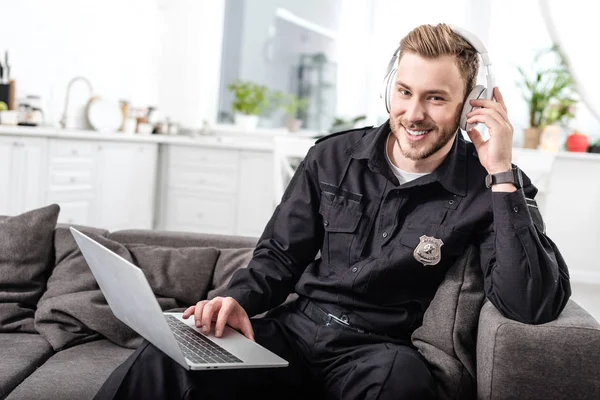 Handsome policeman sitting on sofa with laptop and listening to music — Stock Photo