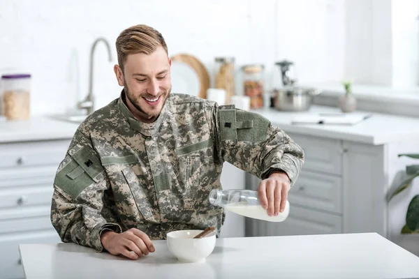 Усміхнений військовий виливає молоко в миску з кукурудзяними пластівцями — стокове фото