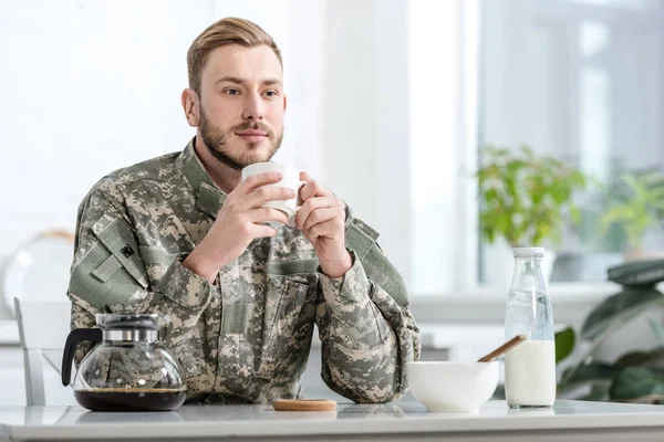 Handsome man in military uniform drinking coffee at kitchen table — Stock Photo