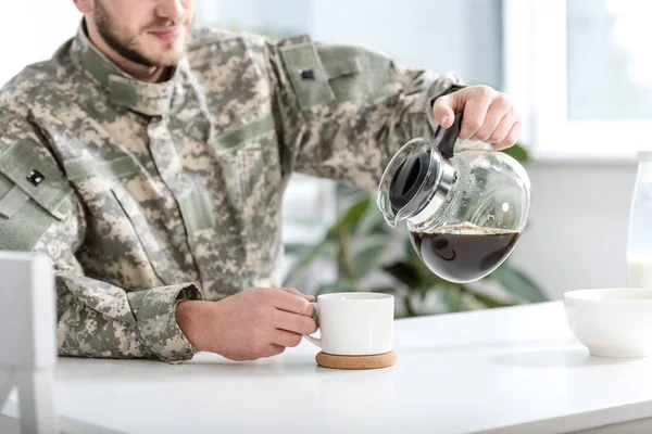 Abgeschnittene Ansicht eines Mannes in Tarnuniform, der in der Küche Kaffee in Tasse einschenkt — Stockfoto