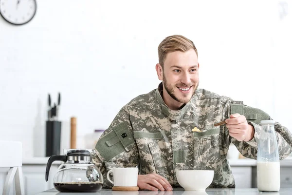 Smiling man in military uniform eating cornflakes at kitchen — Stock Photo