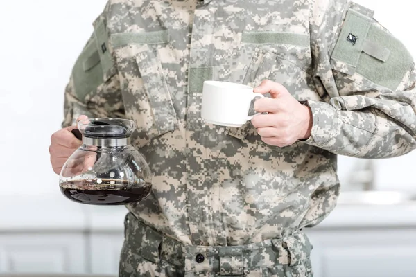 Vista parcial del soldado del ejército sosteniendo taza de café y olla en la cocina - foto de stock