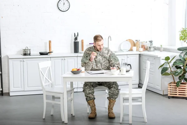 Soldat de l'armée assis à la table de cuisine et prenant le petit déjeuner à la maison — Photo de stock