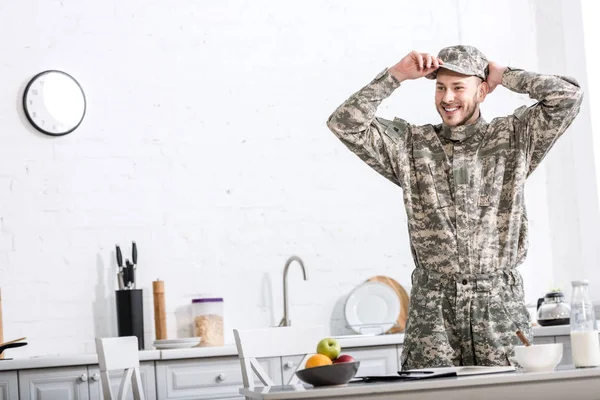 Army soldier putting on hat in kitchen — Stock Photo