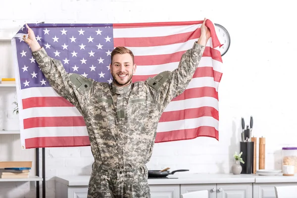 Красивый солдат, стоящий, смотрящий в камеру и гордо держащий американский флаг — стоковое фото