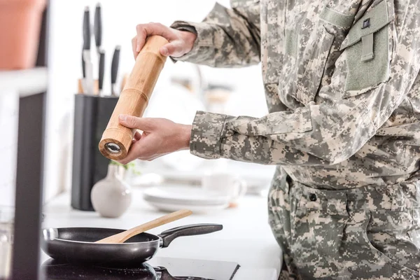 Обрезанный вид армейского солдата, использующего перец горшок во время приготовления пищи на кухне — стоковое фото