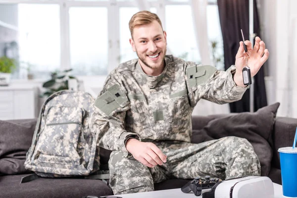 Aufgeregter Armeesoldat sitzt zu Hause auf Couch, blickt in die Kamera und hält Schlüssel in der Hand — Stockfoto
