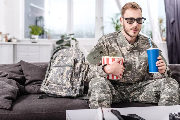 Красивый солдат в трехмерных очках на диване смотрит фильм с попкорном и газировкой — стоковое фото