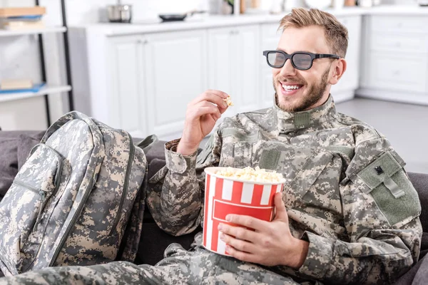 Lächelnder Soldat in Militäruniform mit 3D-Brille, Popcorn essen und Film auf der Couch ansehen — Stockfoto