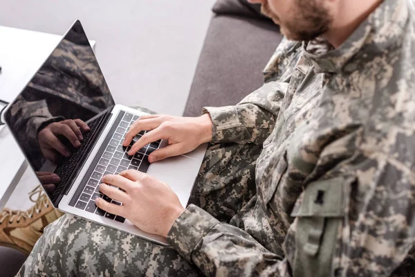 Partial view of army soldier using laptop on couch — Stock Photo