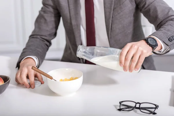 Vista recortada del empresario vertiendo leche en un tazón de cereal en la mesa de la cocina - foto de stock