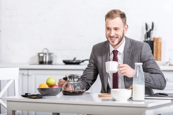 Sonriente empresario bebiendo café en la mesa de la cocina - foto de stock