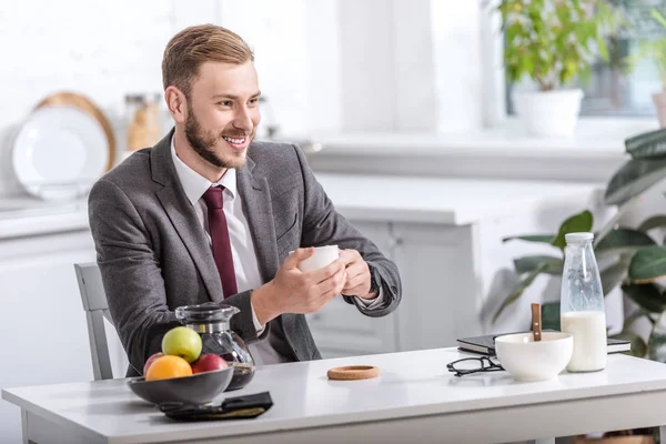 Bonito homem de negócios tomando café da manhã e beber café na mesa da cozinha — Fotografia de Stock