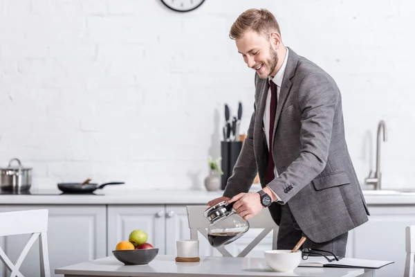 Uomo d'affari sorridente versando caffè filtrato in tazza in cucina — Foto stock