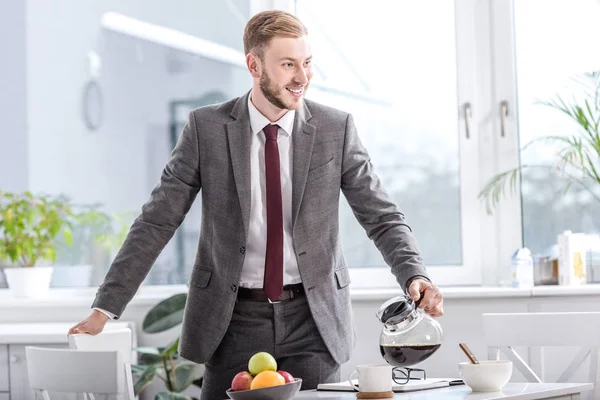 Smiling businessman pouring filtered coffee in cup at kitchen — Stock Photo