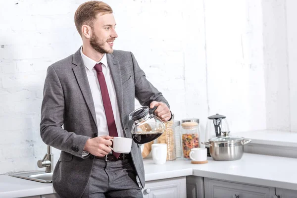Bell'uomo d'affari versa caffè filtrato in tazza in cucina e distoglie lo sguardo — Foto stock