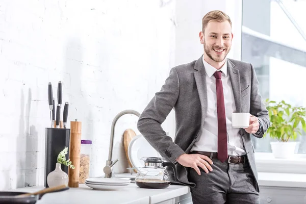 Uomo d'affari sorridente bere caffè in cucina e guardando la fotocamera — Foto stock
