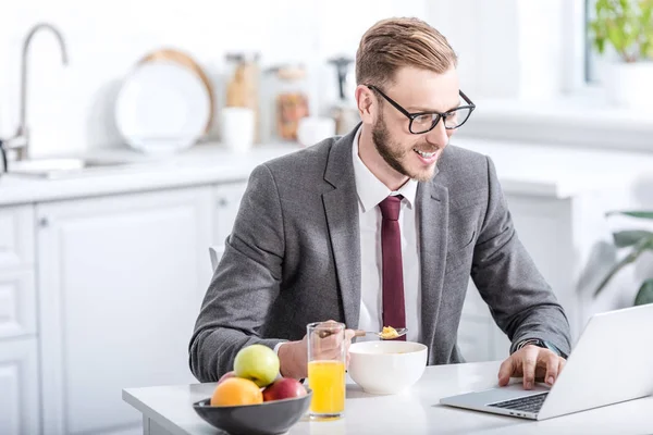 Geschäftsmann arbeitet am Laptop während er in der Küche frühstückt — Stockfoto