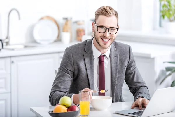 Uomo d'affari che lavora sul computer portatile mentre fa colazione in cucina — Foto stock